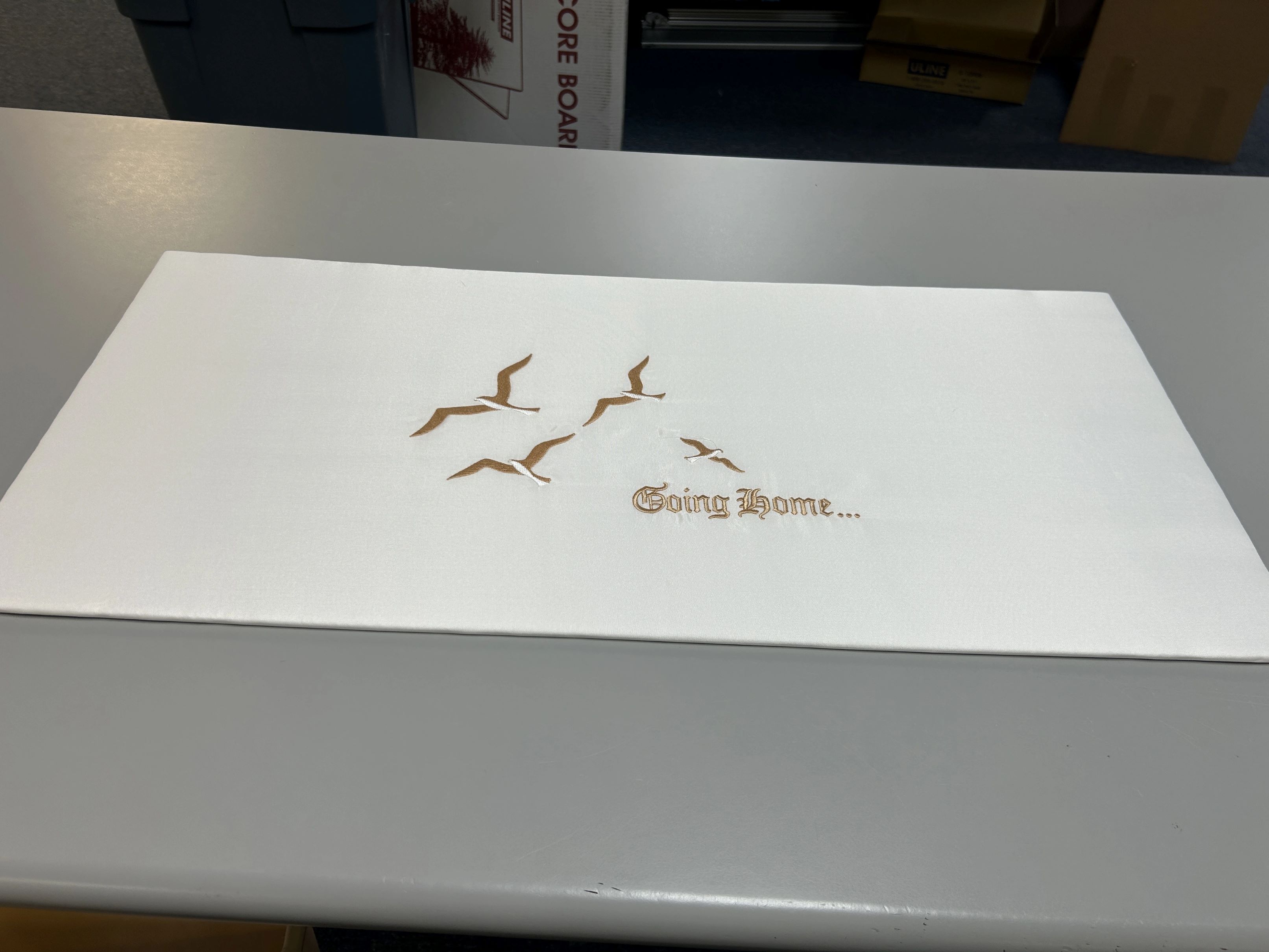 Image of embroidery mounted on a rectangular panel. It says 'Going Home' in gold thread with several flying birds around the text.